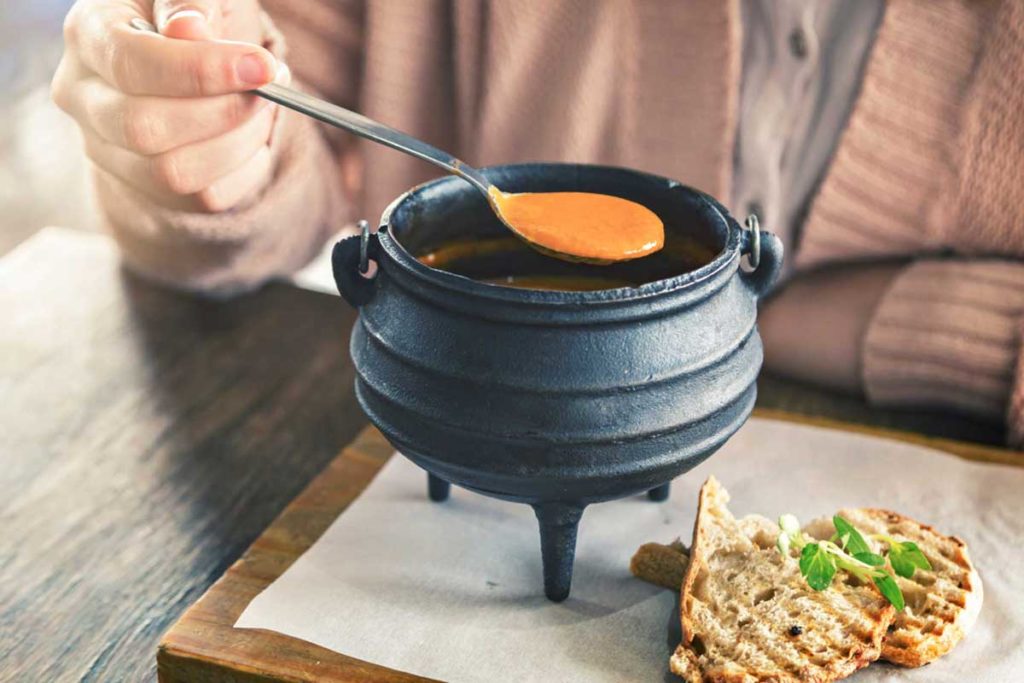 Tomato soup in a small black cauldron on a chopping board with bread