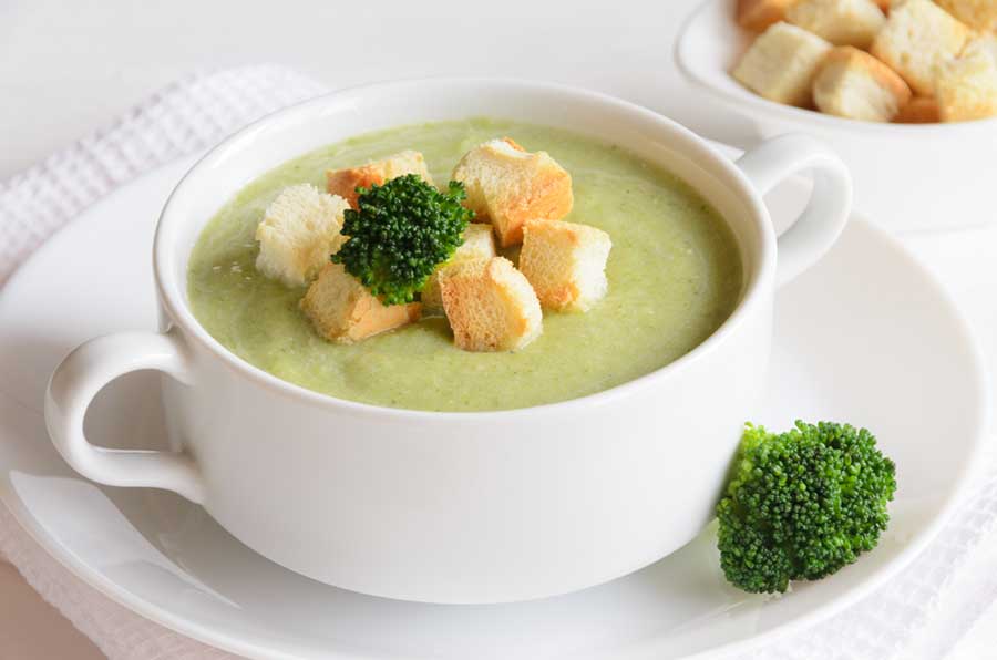 Fresh broccoli cream soup in bowl served with croutons and topped with broccoli on white kitchen towel