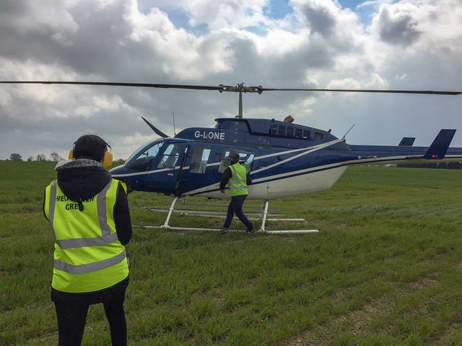 Two people in hi-vis jackets boarding a dark blue helicopter