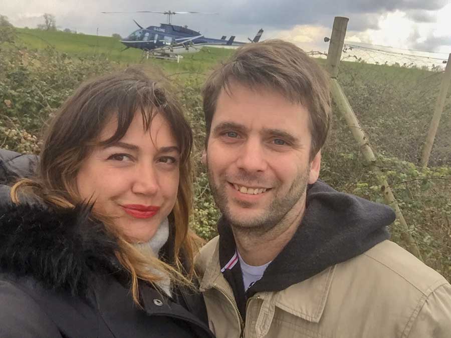 A man and a woman smiling with a dark blue helicopter in the background