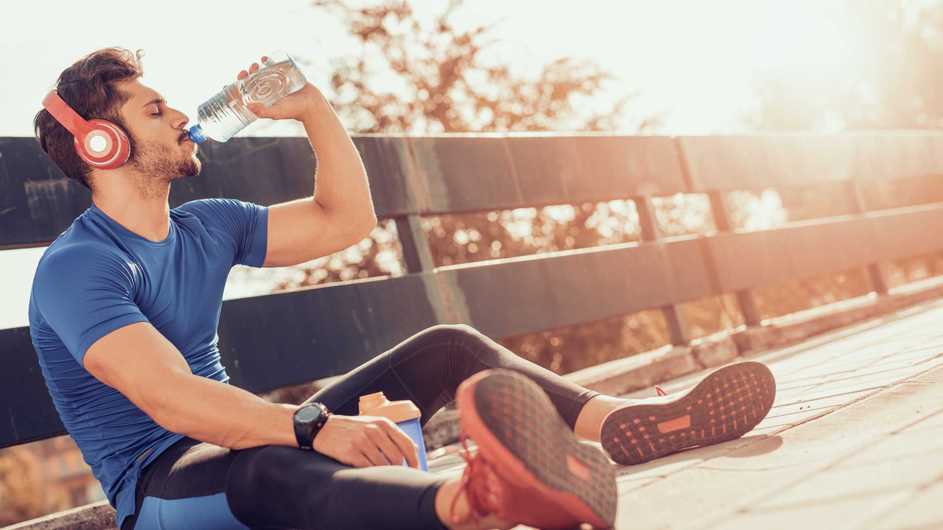 Portrait of young man drinking some water from a bottle while sitting and resting after training