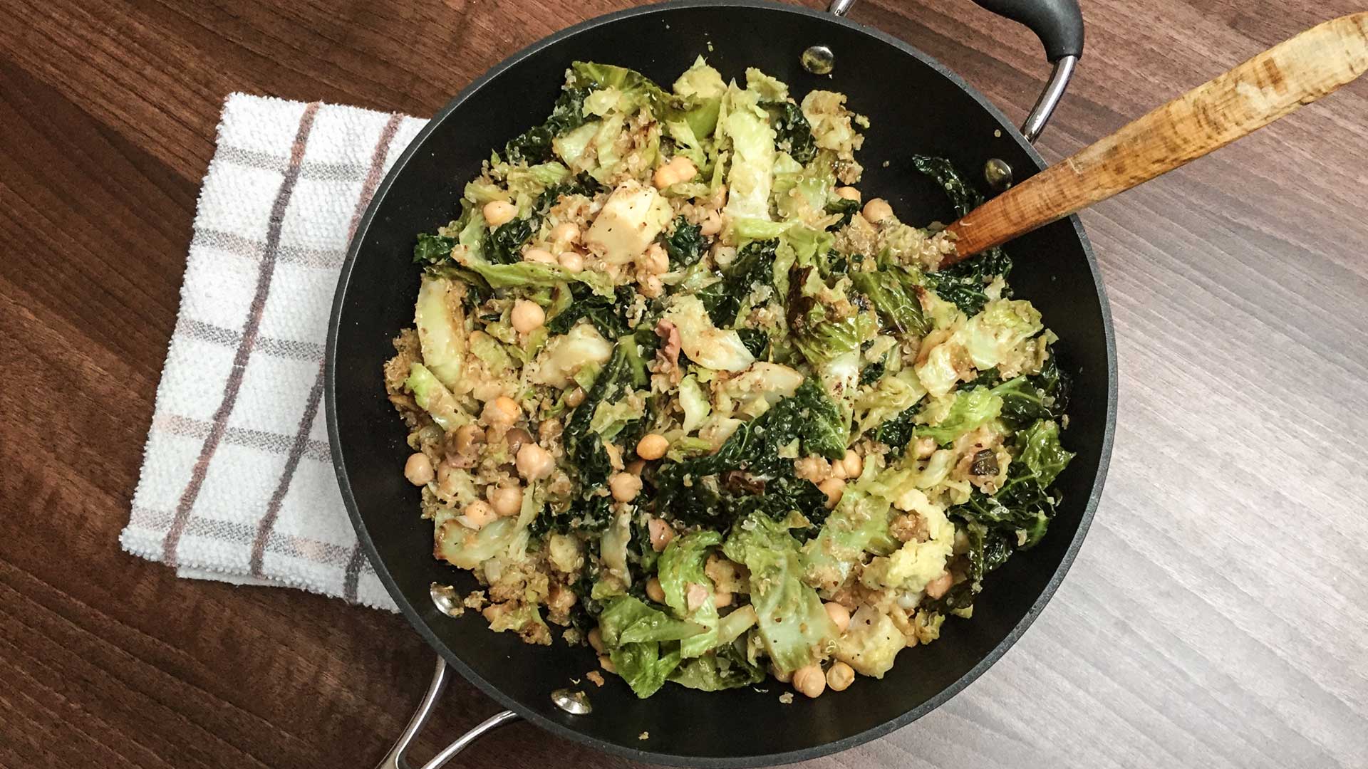 Toasted lemon quinoa cabbage salad in a large skillet on wooden dinner table with kitchen towel