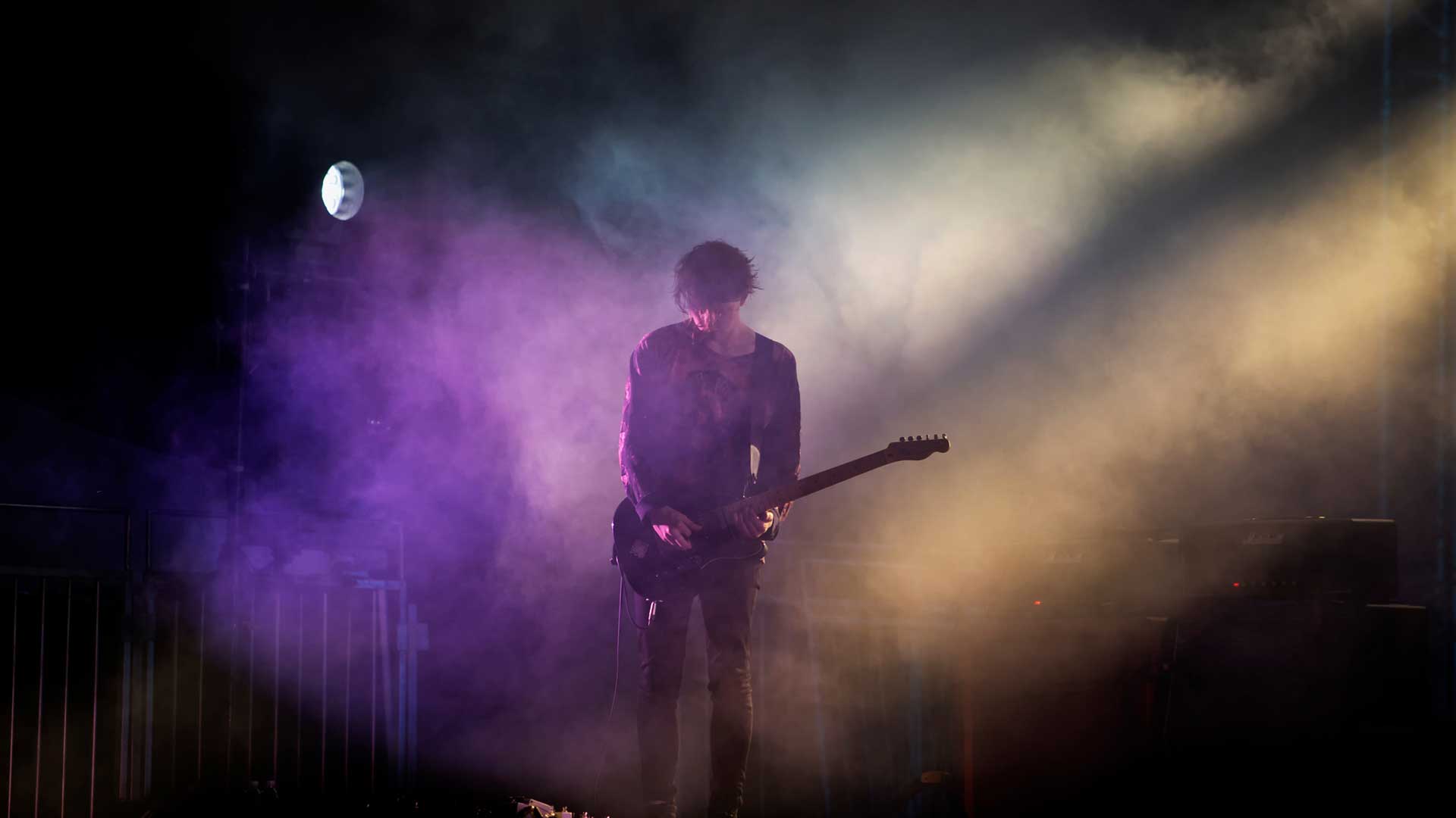 Mogwai on stage, guitarist playing lit with purple and yellow light surrounded by smoke