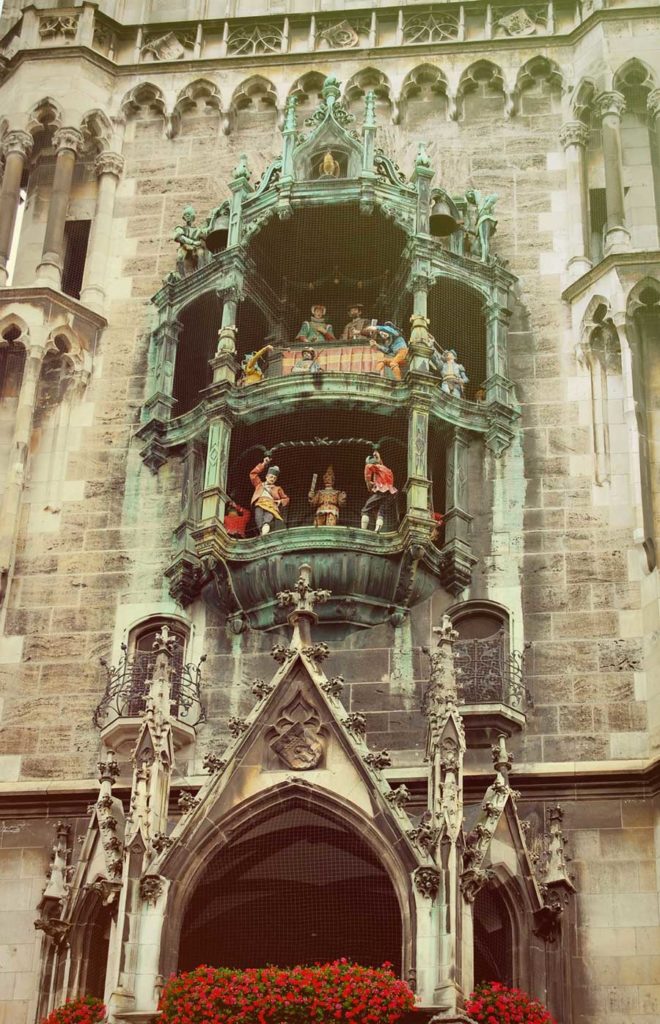 A close up of an old grey Gothic building with life-sized mannequins on two balconies