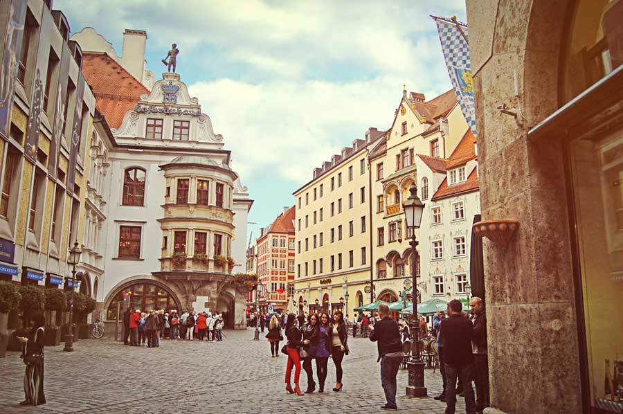A cobbled city square with old buildings surrounding it and small groups of people
