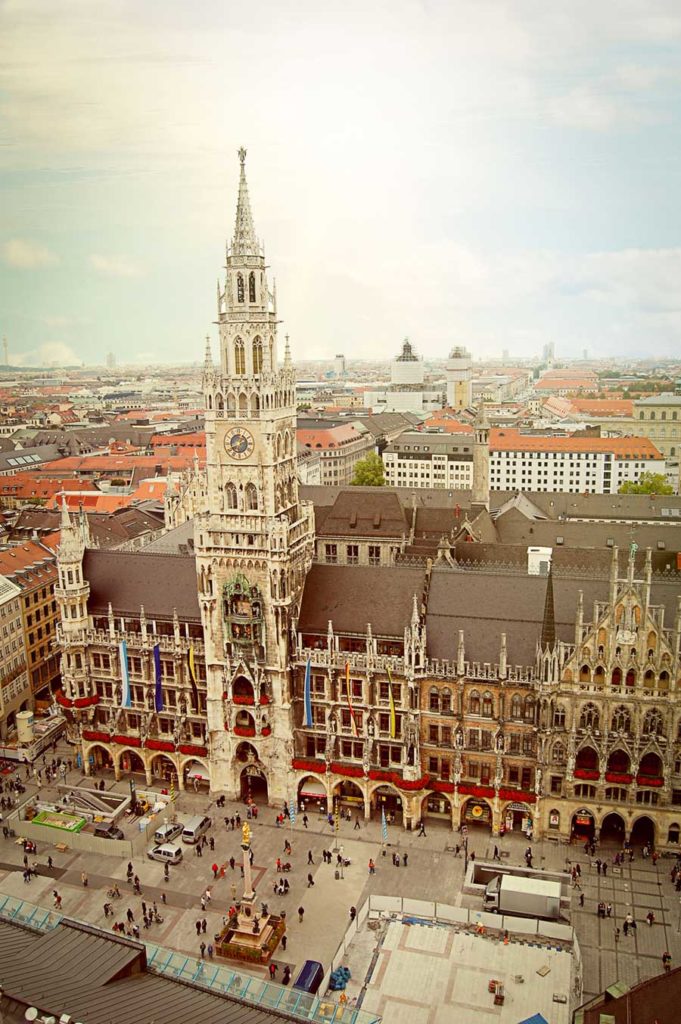 An old, ornate, Gothic building with a tall spire above a city square.