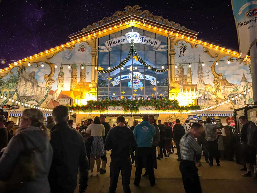 Crowd of people in the foreground with a brightly lit huge beer tent in the background