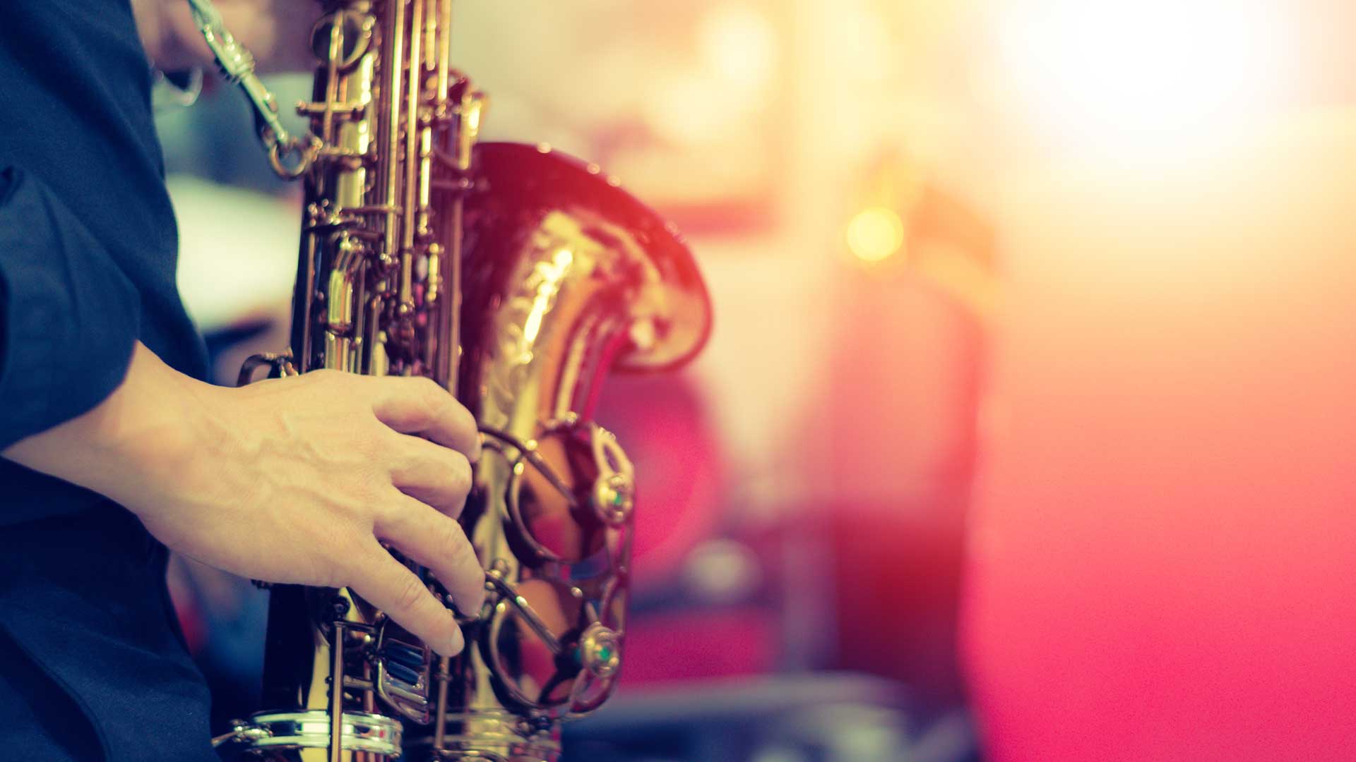 Saxophone held by a musician in a black shirt, against a blurred red background