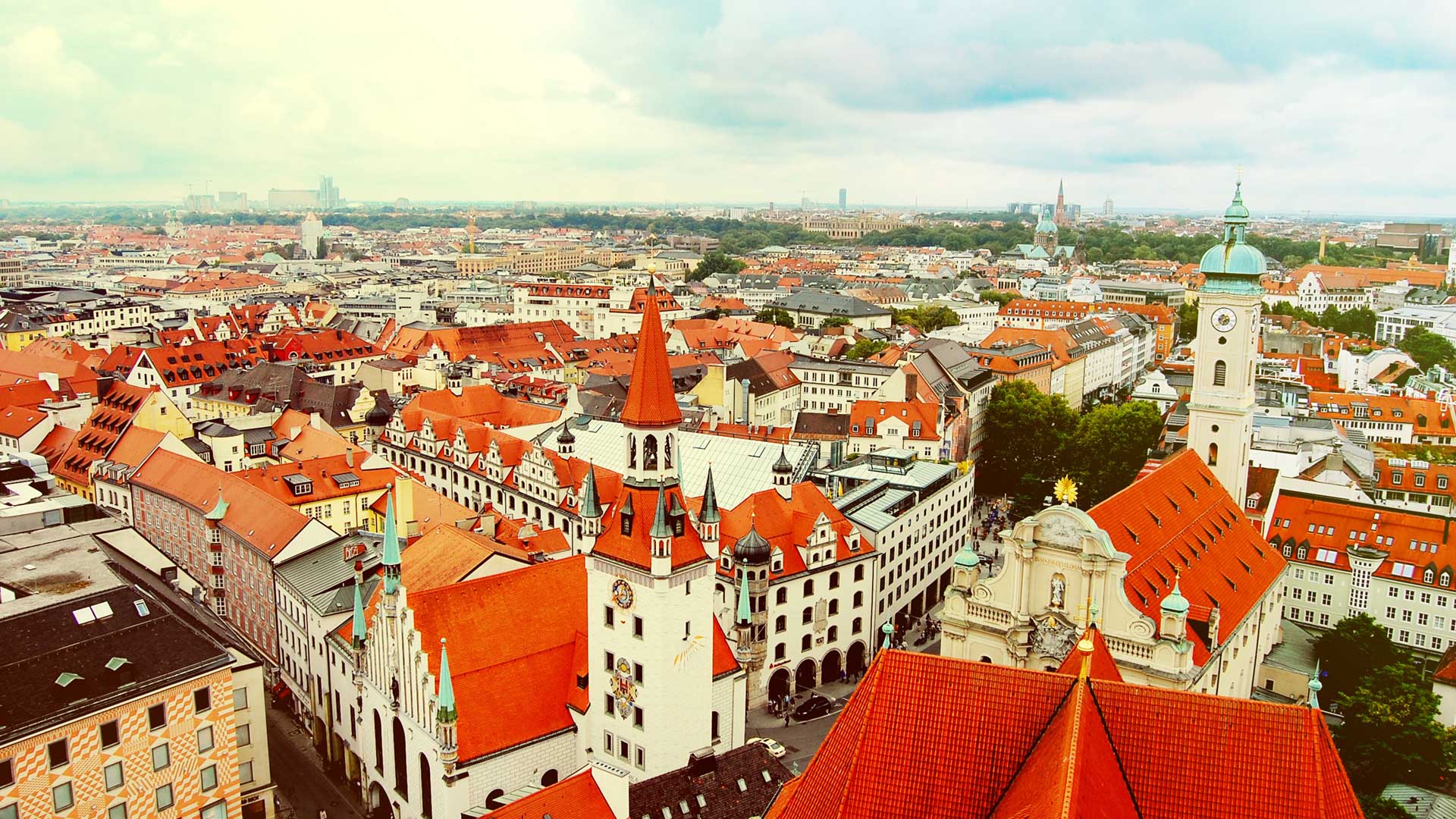 Skyline of Munich from high vantage point, with white buildings with red roofs and a cloudy blue sky