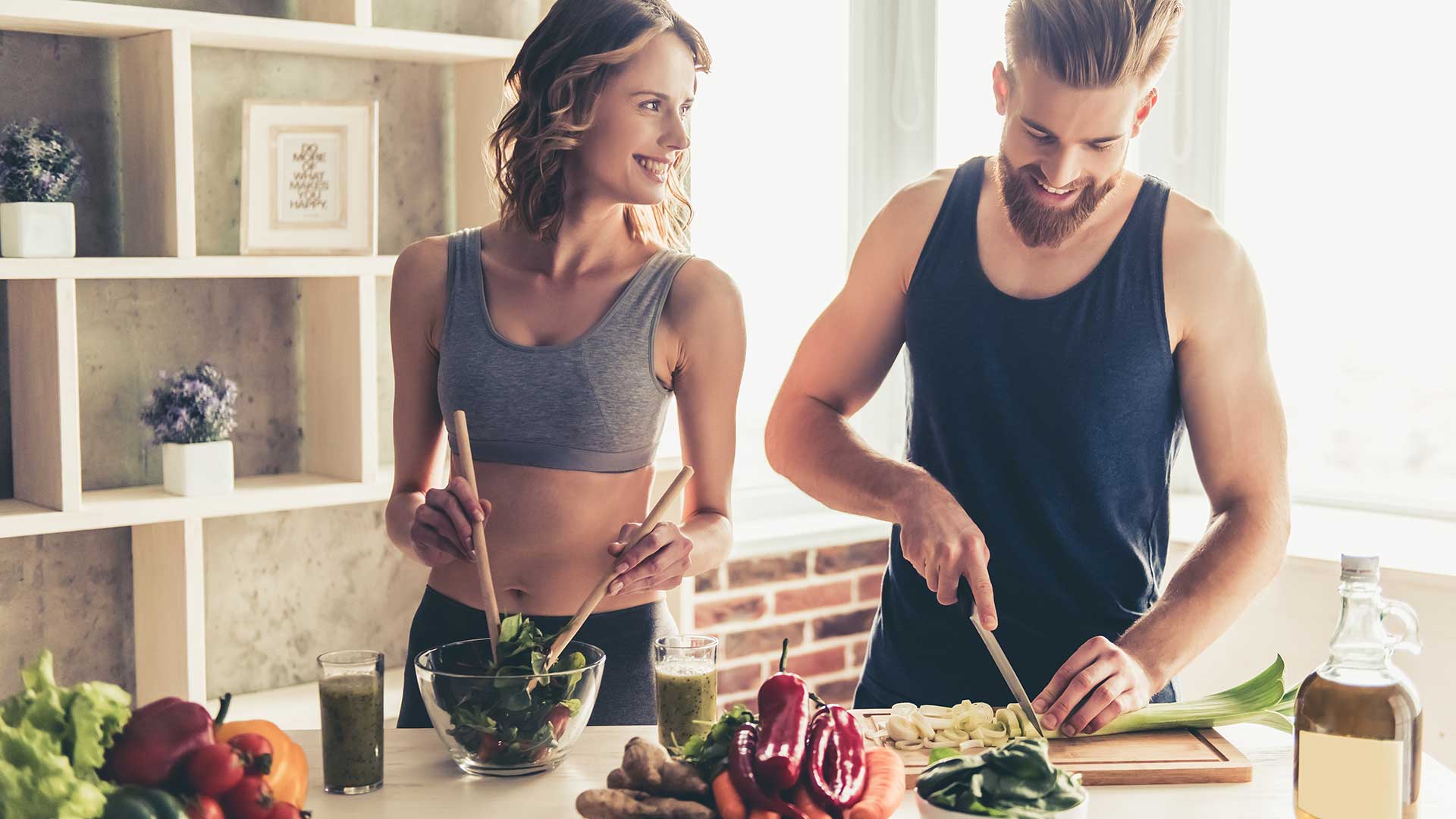 Beautiful young sports people are talking and smiling while cooking healthy food in kitchen at home