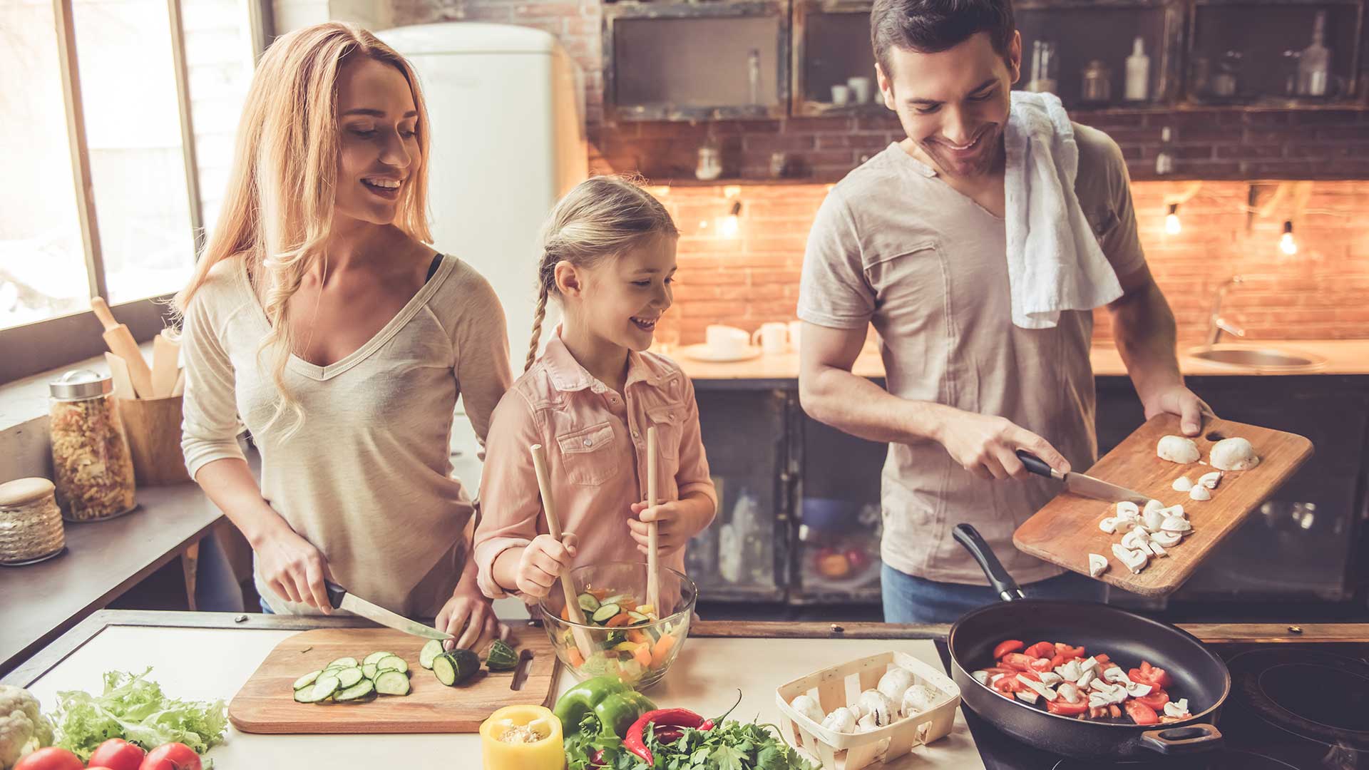 Cute little girl and her beautiful parents are smiling while cooking in kitchen at home