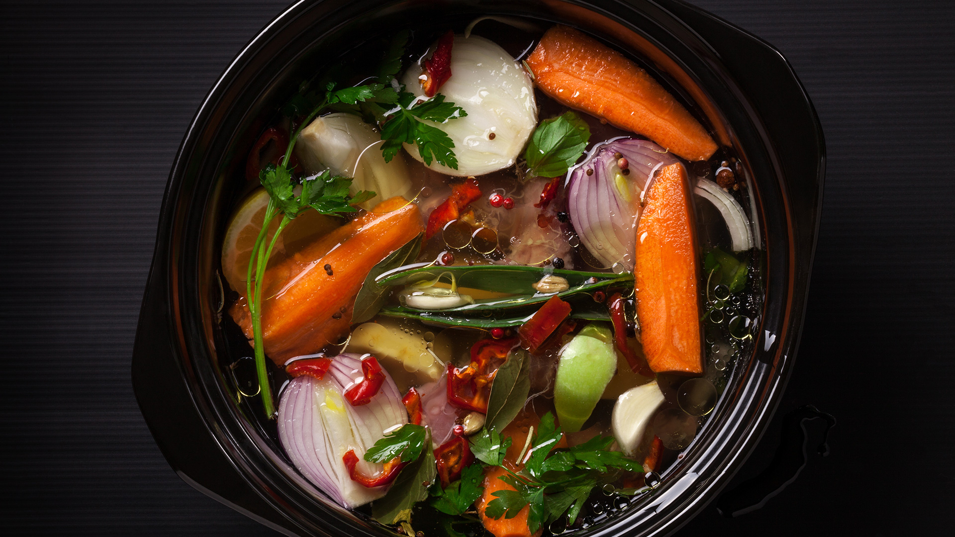 Fresh vegetable soup in a pot on black background