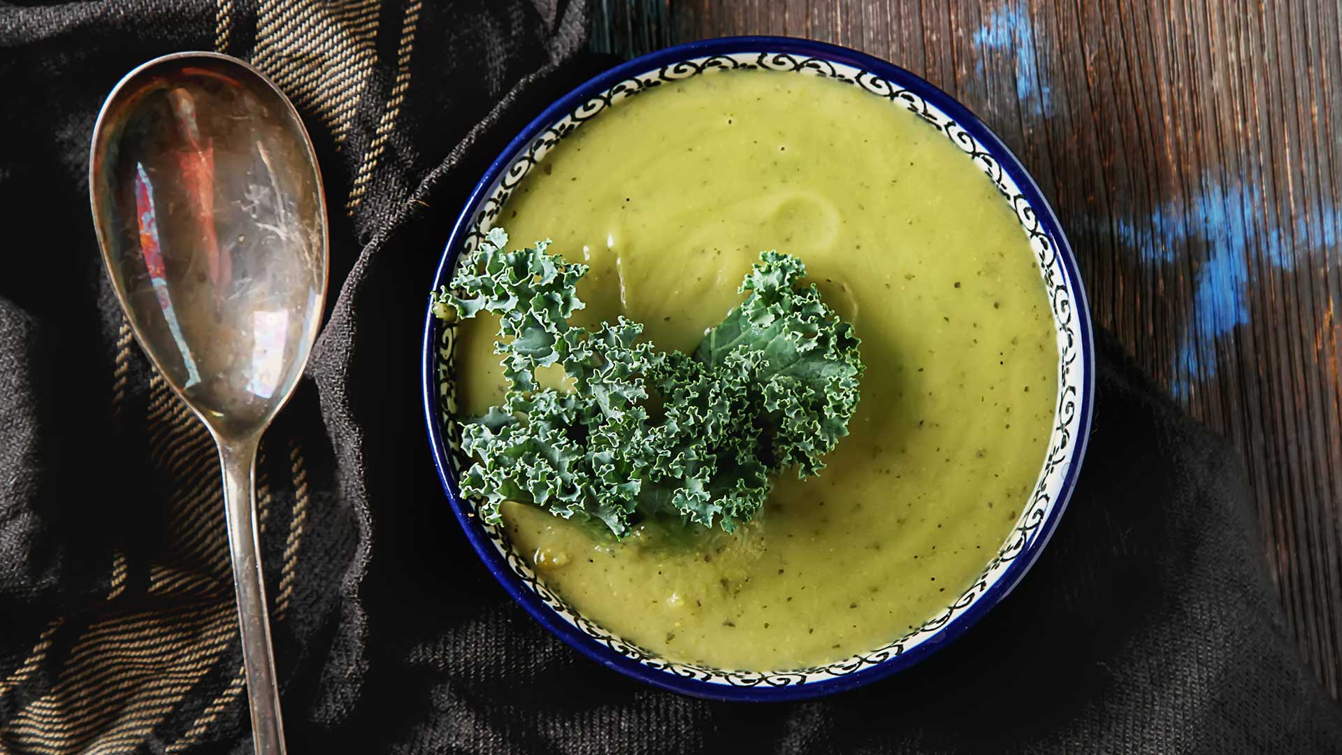 Classic pea puree soup in a blue plate with a spoon, Kale cabbage. Dark wood background