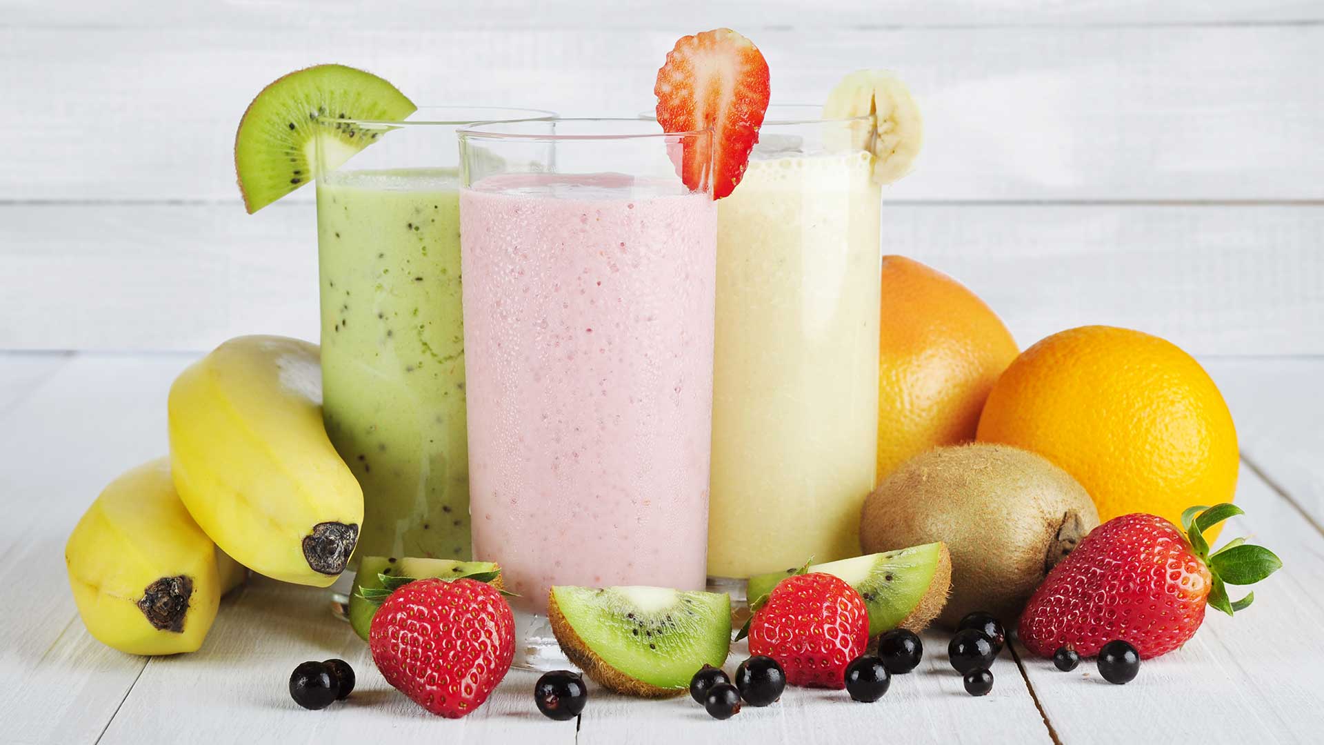 kiwi, strawberry and banana smoothies in a glass with fruits around them on a white wooden table