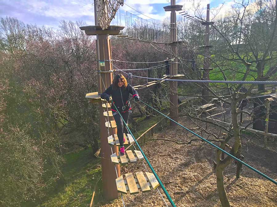 Woman climbing between pillars on a rope and wood bridge