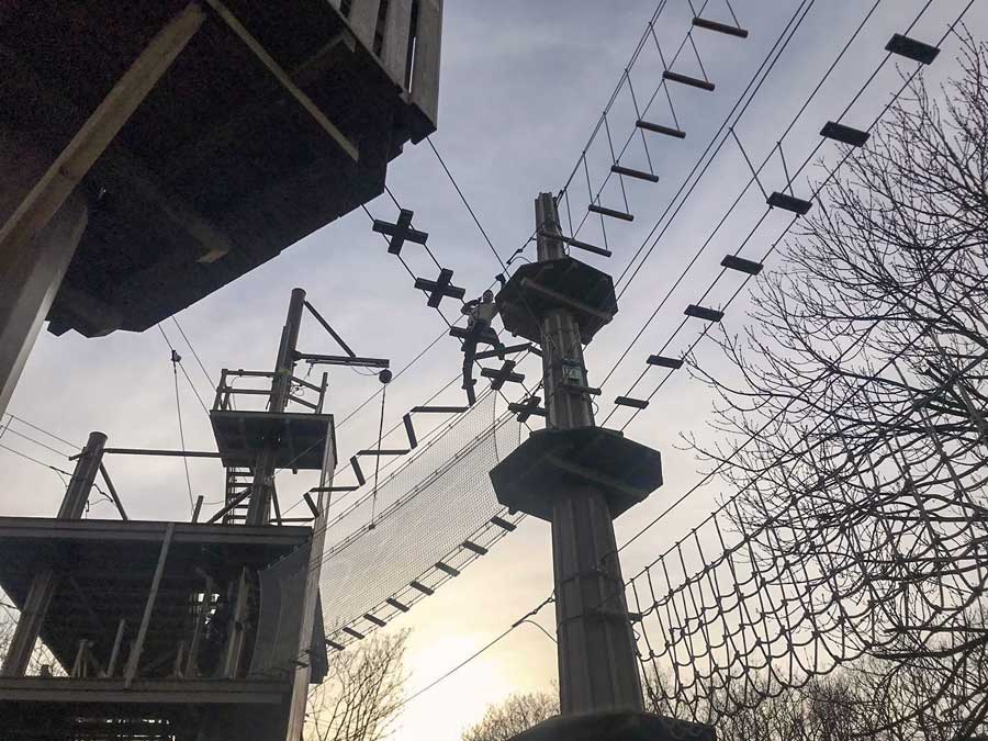 Man climbing on rope bridges high above wooden structures