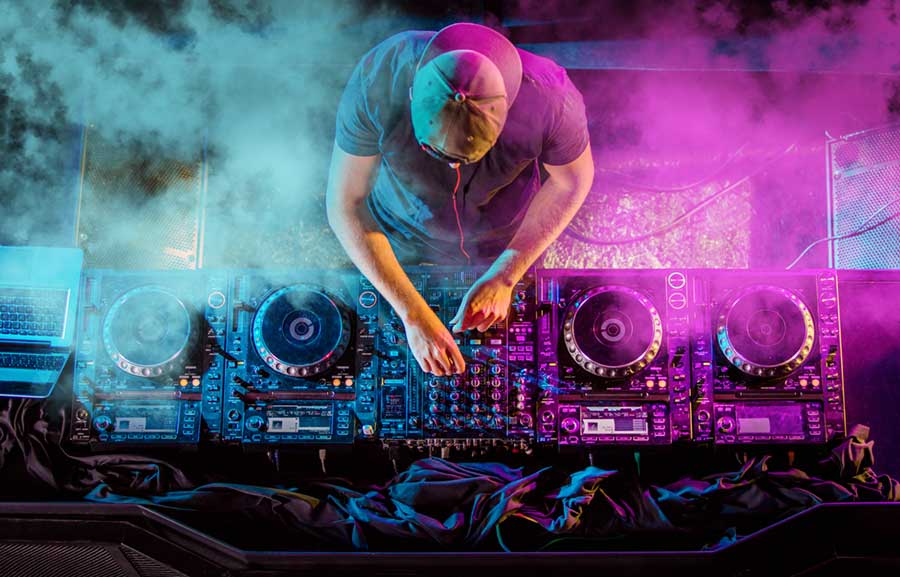 Top down view of a DJ at the turntable, lit by blue and purple lights and surrounded by smoke