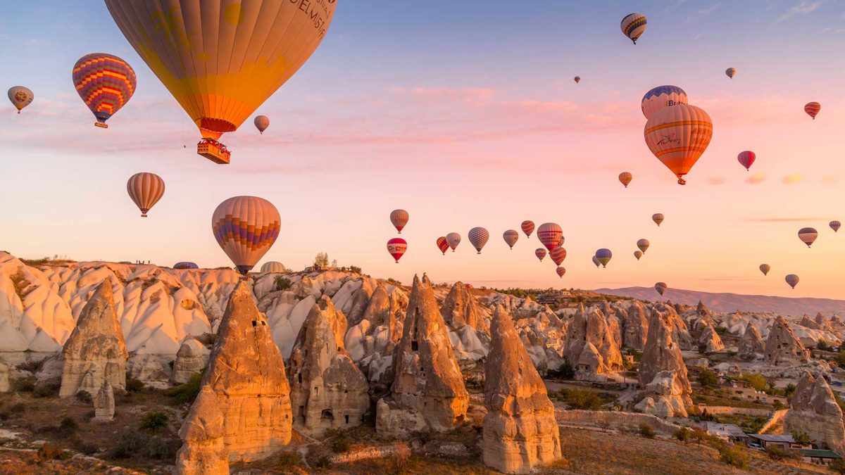 Hot air balloons filled with tourists during a pink sunrise floating along valleys of Göreme National Park