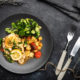 Baked Lemon & Herb Fish With Cherry Tomatoes on black plate with black dinner table and cutlery set