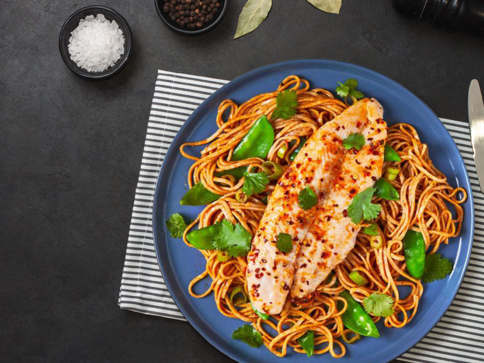 fish with noodles in blue plate on black table