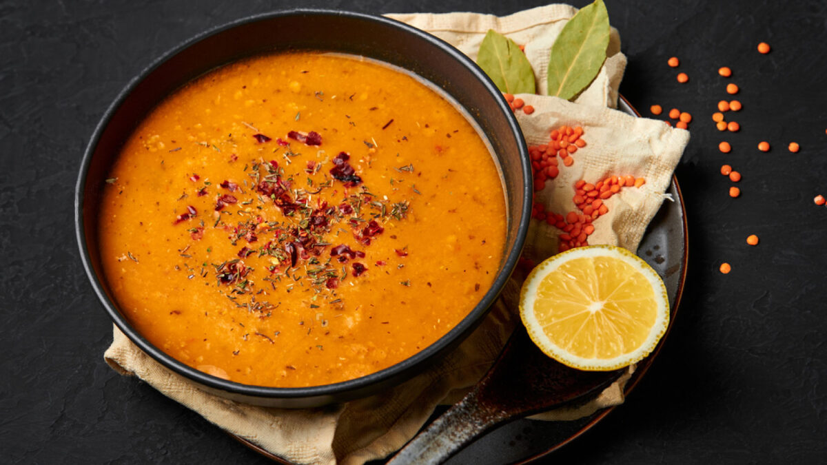 Classic Turkish Ezogelin soup in a black plate with a spoon, lemon, lentils and bayleaf. Dark background